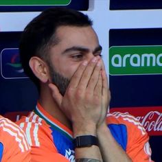 a man covers his face with his hands while sitting in front of a soccer field