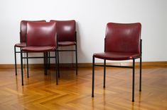 three red leather chairs sitting on top of a hard wood floor next to a white wall