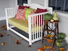 a white bench sitting on top of a porch next to a green chair and some pumpkins