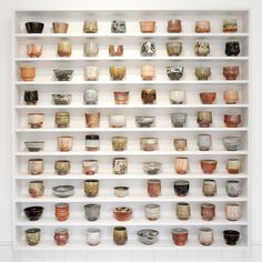 many bowls are arranged on the shelves in this white display case that is filled with cups and saucers