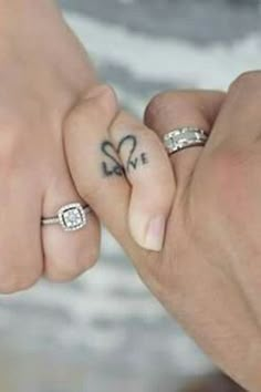 two people holding hands with tattoos on their fingers and the words love written on them