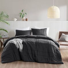 a bed with black and white comforters in a room next to a plant on the floor