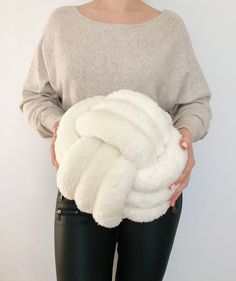 a woman in black pants holding a white blanket over her stomach and wearing a gray sweater