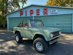 an old pick up truck is parked in front of a large blue building with the word piper on it