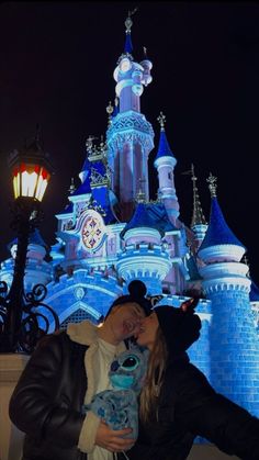 two people kissing in front of a castle at night