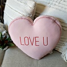 a pink heart shaped pillow sitting on top of a couch next to pillows and flowers