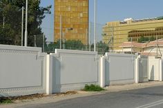 an empty street next to a fence with a tall building in the background