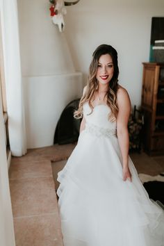 a woman in a white wedding dress standing next to a fireplace and looking at the camera