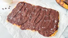 chocolate frosted pastry sitting on top of a piece of parchment paper next to bananas