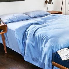 a bed with blue sheets and pillows in a bedroom next to a lamp on a table