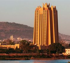 a very tall building sitting on the side of a river next to a large hill