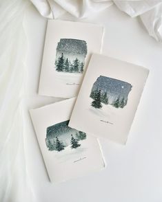 three watercolor paintings of trees in the snow on white paper next to a blanket