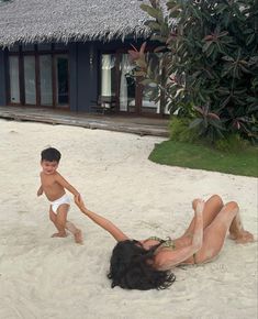 two children playing in the sand on a beach with a hut and pool behind them