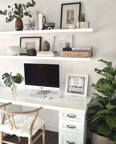 a white desk topped with a computer monitor next to a plant and potted plants