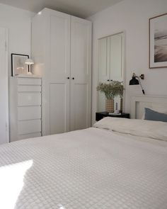 a white bed sitting in a bedroom next to a dresser and cupboards on the wall