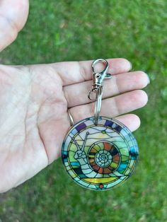 a hand holding a stained glass keychain in it's left hand, with grass in the background