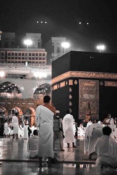 men in white robes standing around the ka'bah at night with lights on