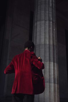 a man in a red jacket standing next to some columns