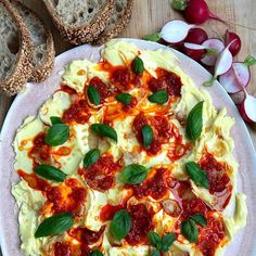 a pizza with basil leaves on it sitting on a plate next to some slices of bread