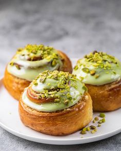 three small pastries on a white plate with pistachios and green icing