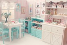 a dollhouse kitchen with pink and blue decor on the walls, white table chairs and shelves filled with cupcakes