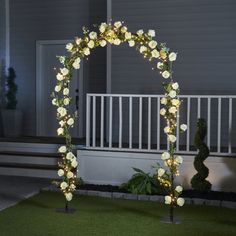 an outdoor wedding arch decorated with white flowers and fairy lights at night in front of a house