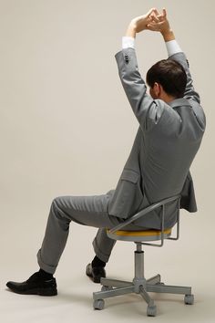 a man in a suit sitting on a chair with his hands up to the side