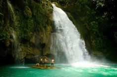 people standing in front of a waterfall while others stand on the rafts watching them