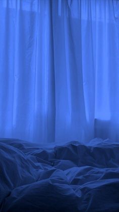 an unmade bed with blue sheets and curtains