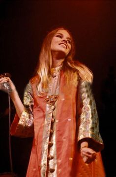 a woman in an orange dress holding a microphone and singing into the air with her hands