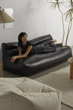 a woman sitting on top of a black couch in a living room next to a lamp