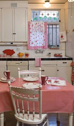 a kitchen with white cabinets and red gingham table cloth on the dining room table