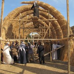 some people are standing around in front of a straw structure with a man on top