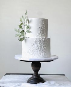 a three tiered white cake sitting on top of a wooden table next to a leafy green plant