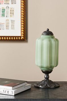 a green glass jar sitting on top of a wooden table next to a framed picture