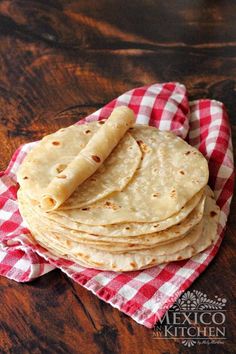 tortillas are stacked on a red and white checkered napkin with a wooden table in the background