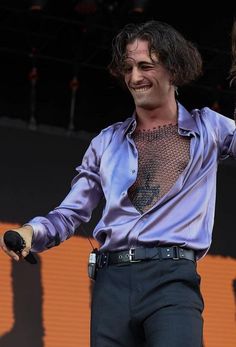 a man with long hair wearing a purple shirt and black pants holding his arms out