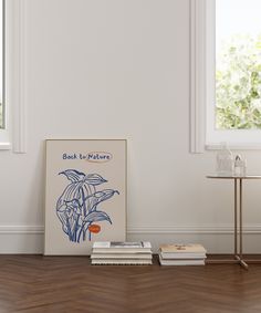 a table with books on it in front of a white wall and two large windows