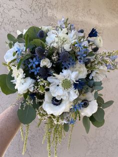 a bouquet of white and blue flowers is held by a person's arm against a wall