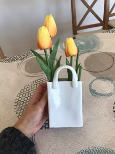 a hand holding a white bag with yellow tulips in it on a table