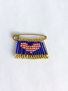 an american flag pin is shown on a white surface with blue beads and gold trim