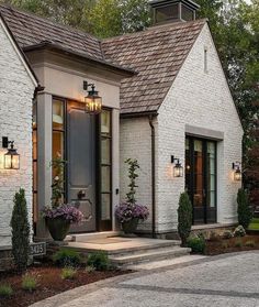 a white brick house with two potted plants on the front porch and stairs leading up to it