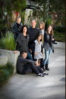 a family posing for a photo in front of some bushes and trees with their arms around each other