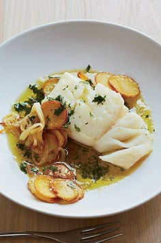 a white plate topped with fish and potatoes on top of a wooden table next to a fork