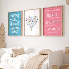 three framed art pieces hang on the wall above a bed in a white room with pink and blue accents