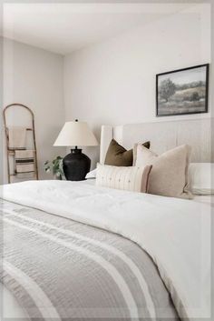 a bed with white linens and pillows in a bedroom next to a painting on the wall