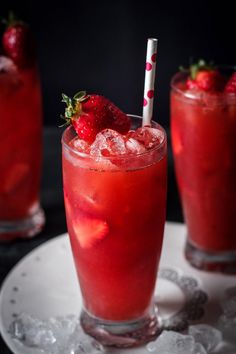 two glasses filled with red liquid and topped with strawberries on a white platter