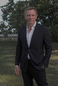 a man in a suit is standing on the grass with his hands in his pockets