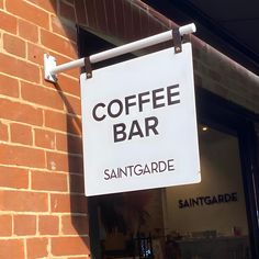 a coffee bar sign hanging from the side of a brick building