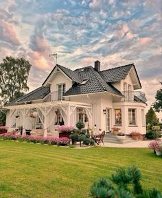 a large white house sitting in the middle of a lush green field with lots of flowers